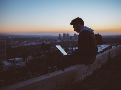 Man sitting on ledge with computer overlooking a city