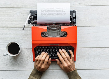 Hands typing on an orange typewrite
