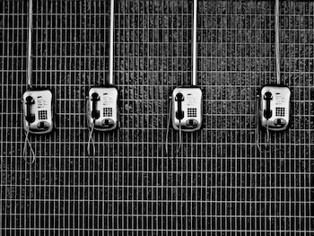 Black and white image of several old pay phones in a row on a wall
