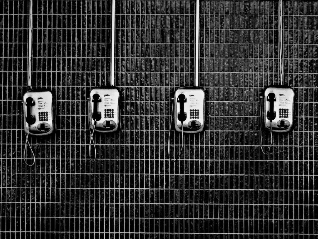Black and white image of several old pay phones in a row on a wall